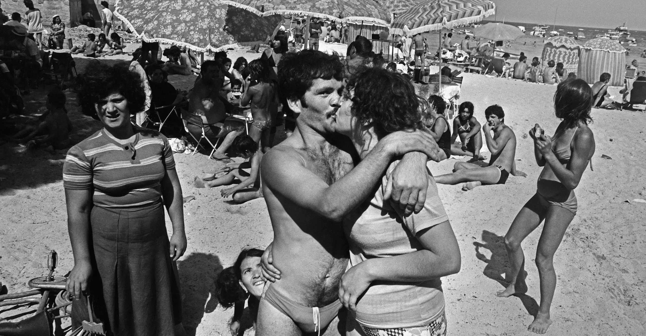 Black and white photo of a couple kissing and embracing on a busy beach