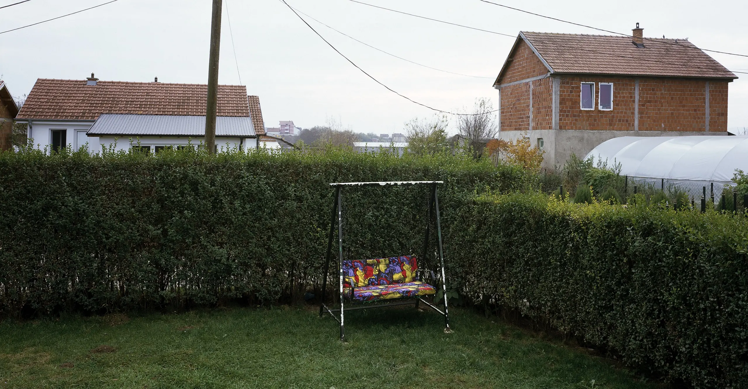 Colour photograph of a garden with an outdoor garden sofa in the corner, the image states ‘Nezir Mirena 21.04.1999’