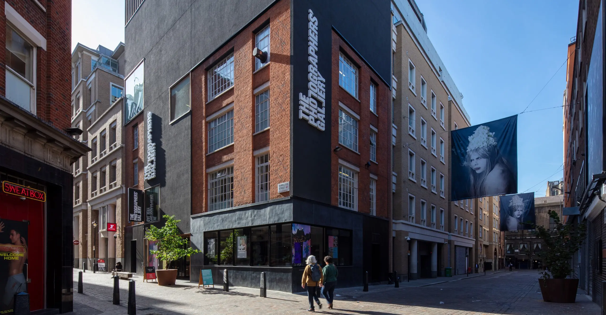 Colour photograph of the exterior corner facade of The Photographers' Gallery, with two people walking past.