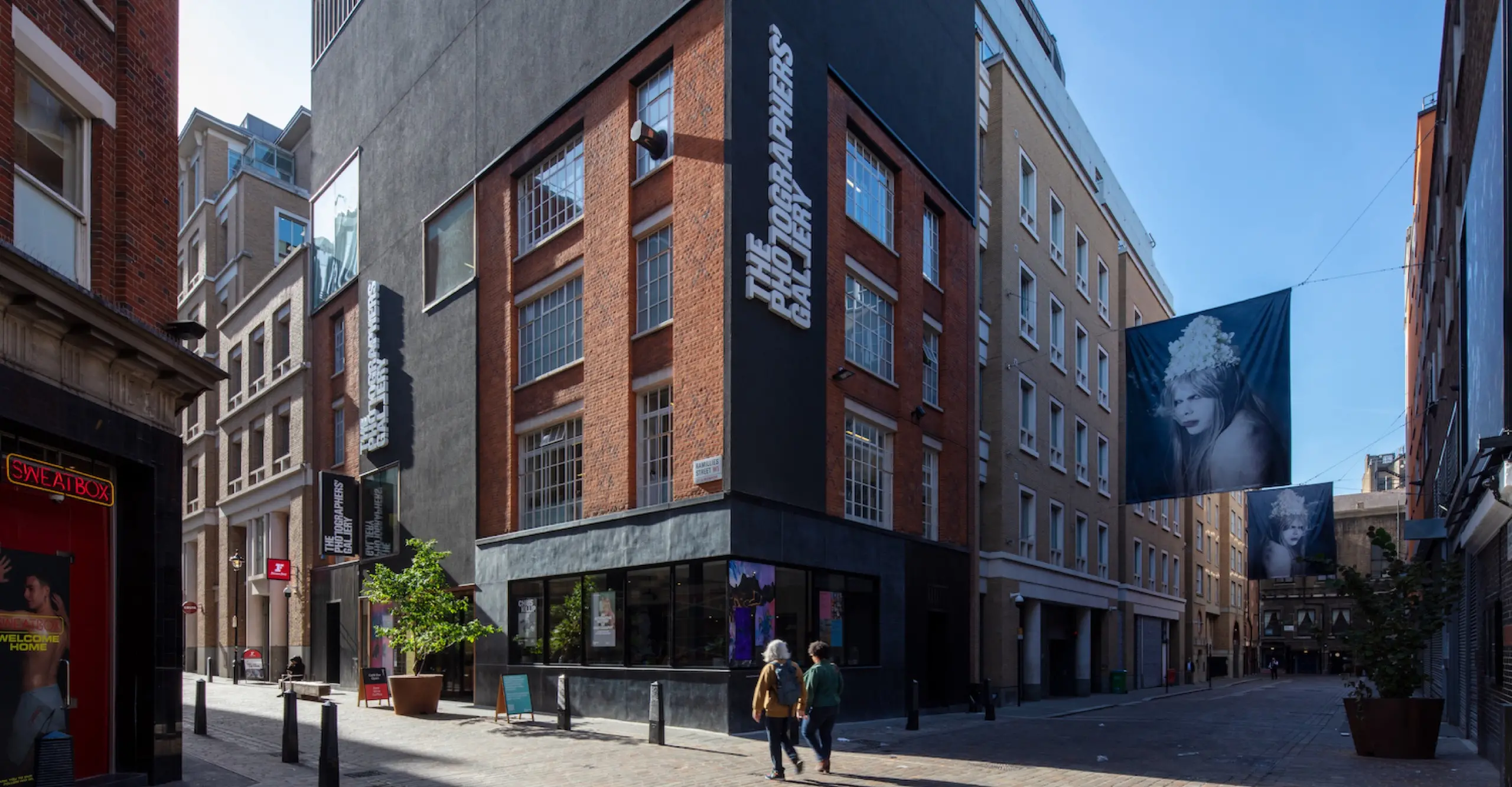 Landscape format image of The Photographers' Gallery on a sunny day with two figures in the foreground walking