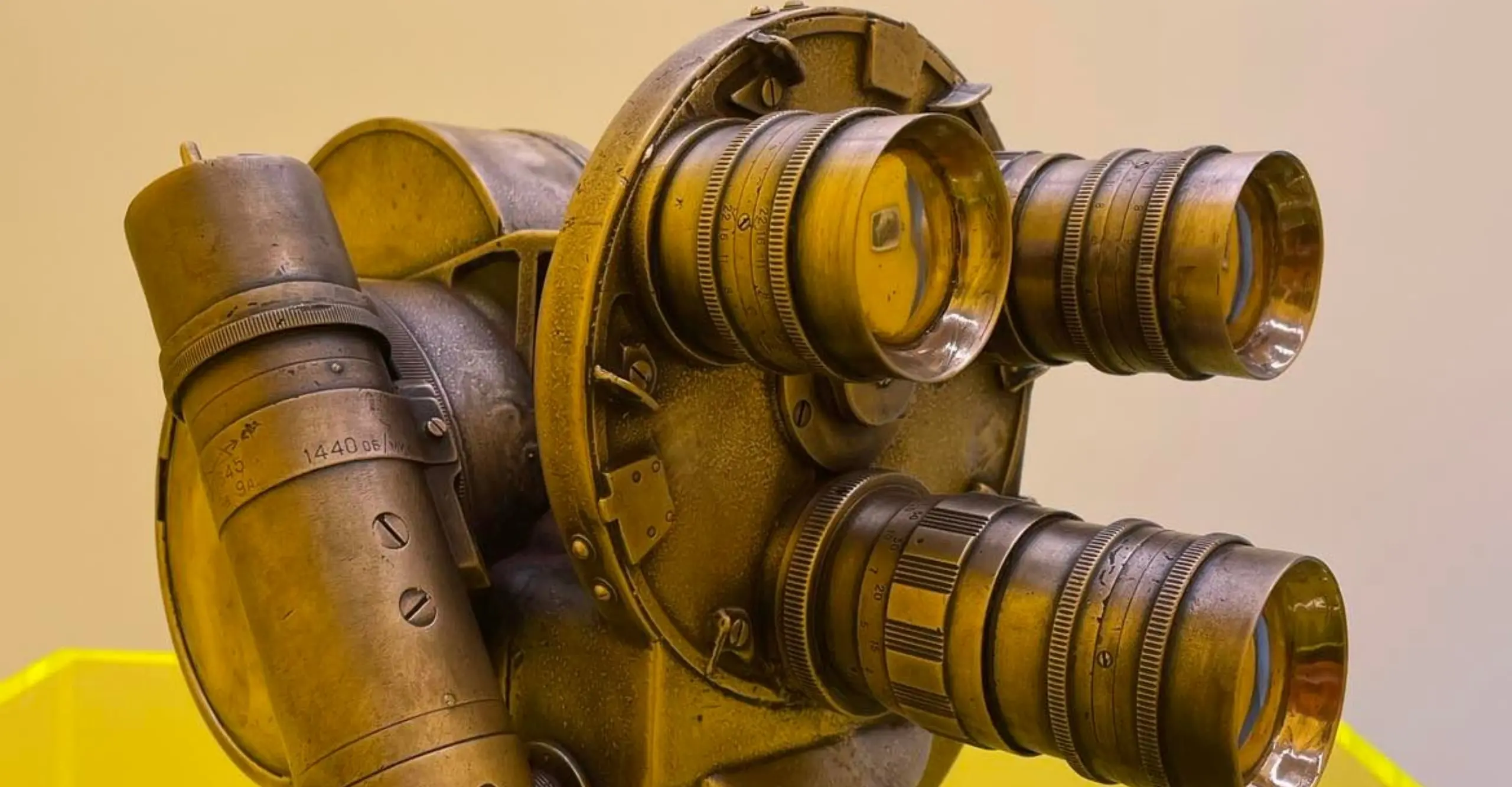 Image of old camera on yellow podium, the camera has three lenses, resembling a face or gas mask