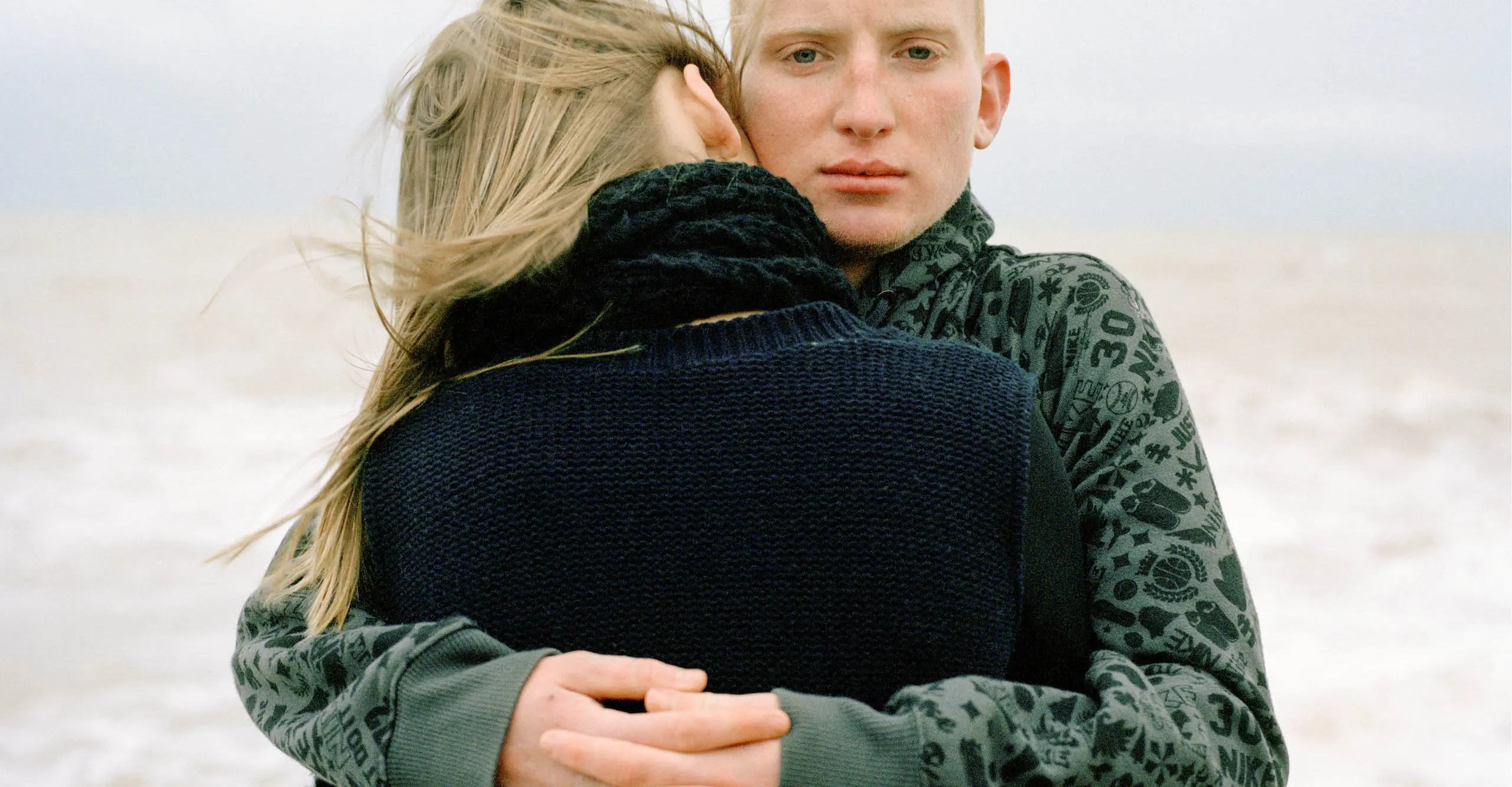 A photograph of two people standing with the sea behind them. 