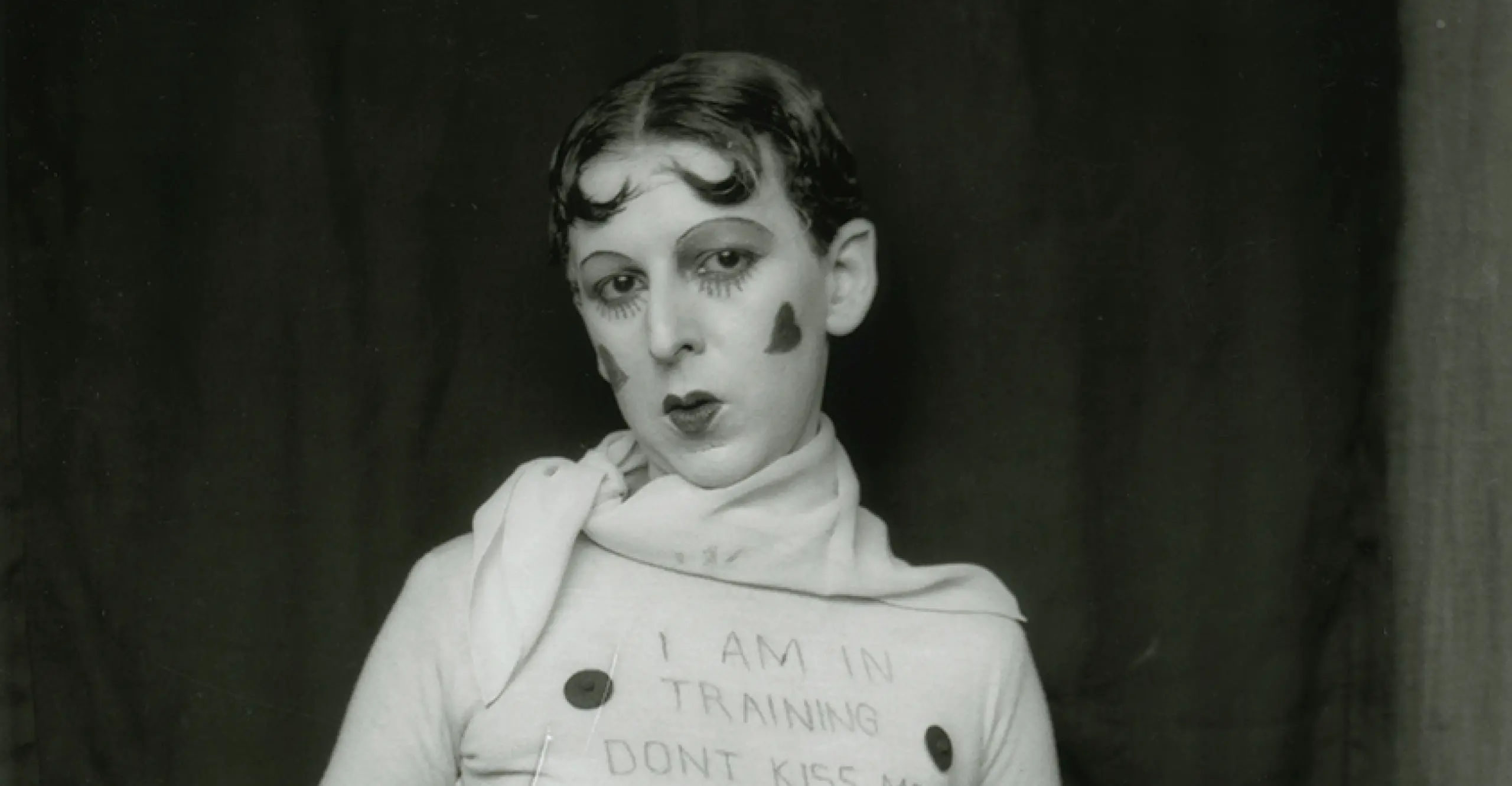 Black and White self-portrait of a Claude Cahun, sitting down wearing a white