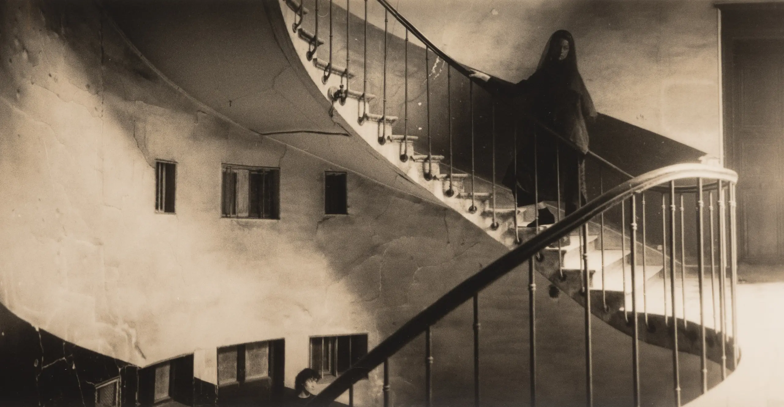 Photograph of a veiled woman on a staircase. She has her head turned back.