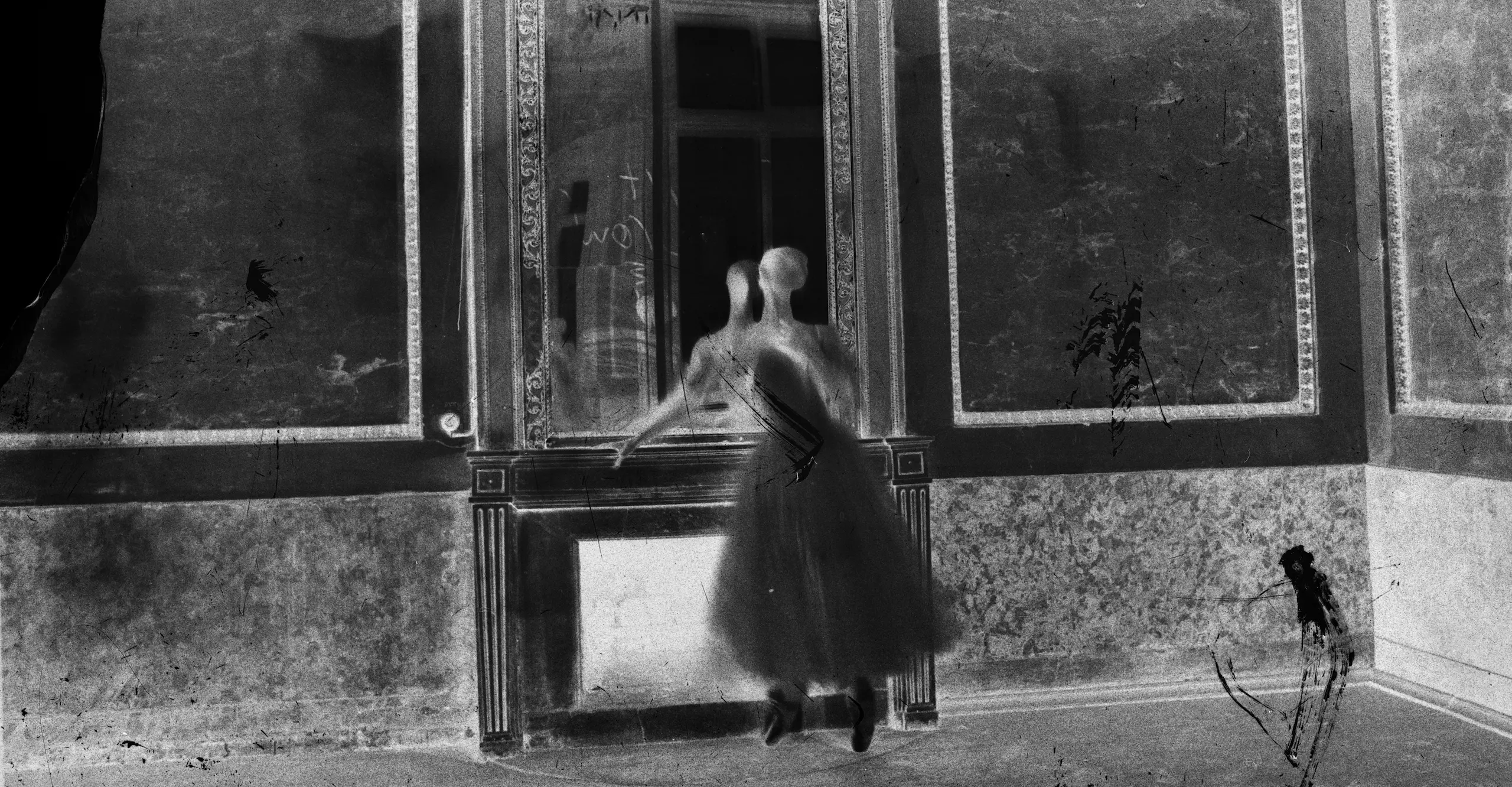 Inverted black and white photograph of a figure standing in a grand room.