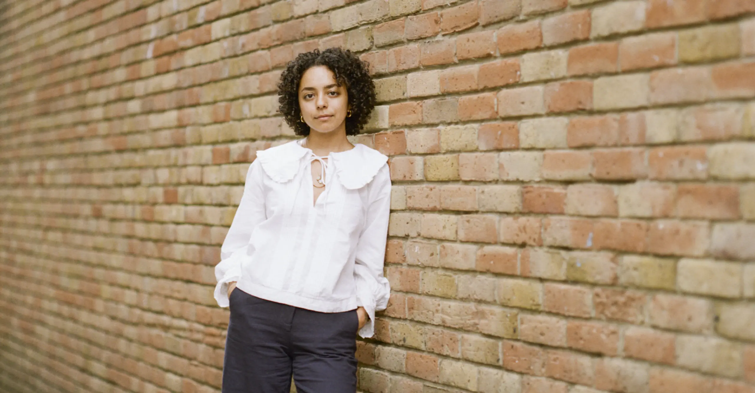 Photograph of woman against brick wall. 