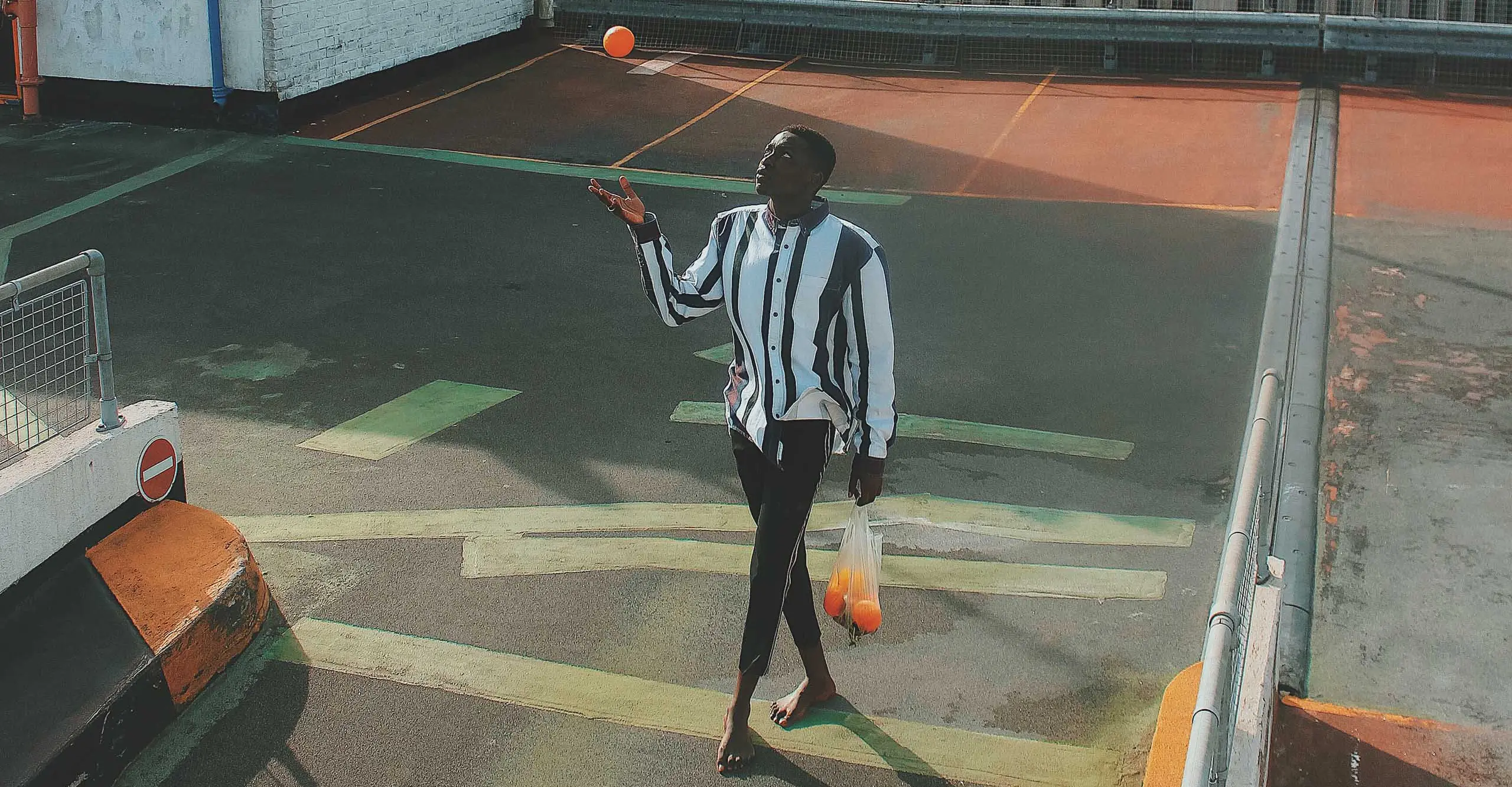 A man walking across a parking lot throwing an orange