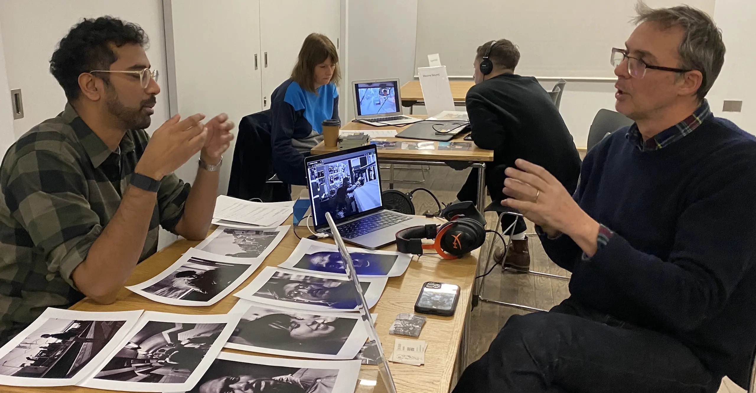 Two people in discussion sit across from each other at a table with photographs spread across it.