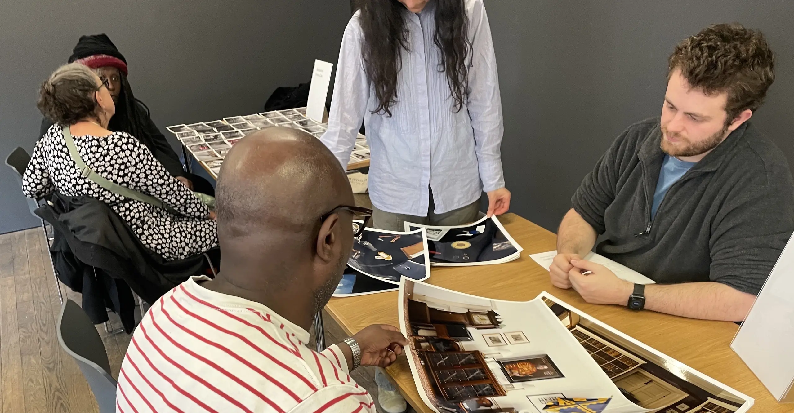 People sit around two tables looking at photographs laid out.