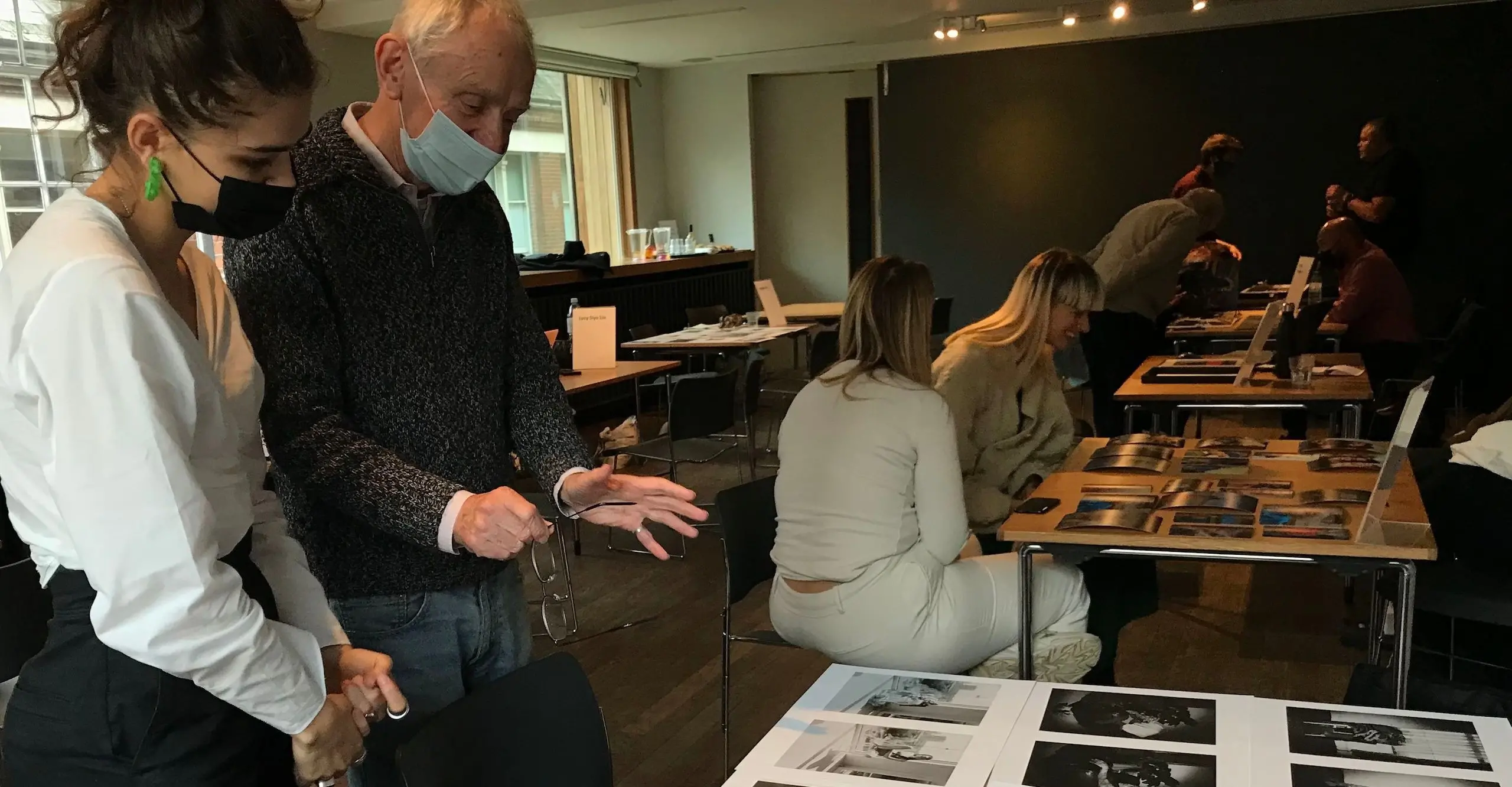 Two people stand in front of a table with photographs spread out on it. 