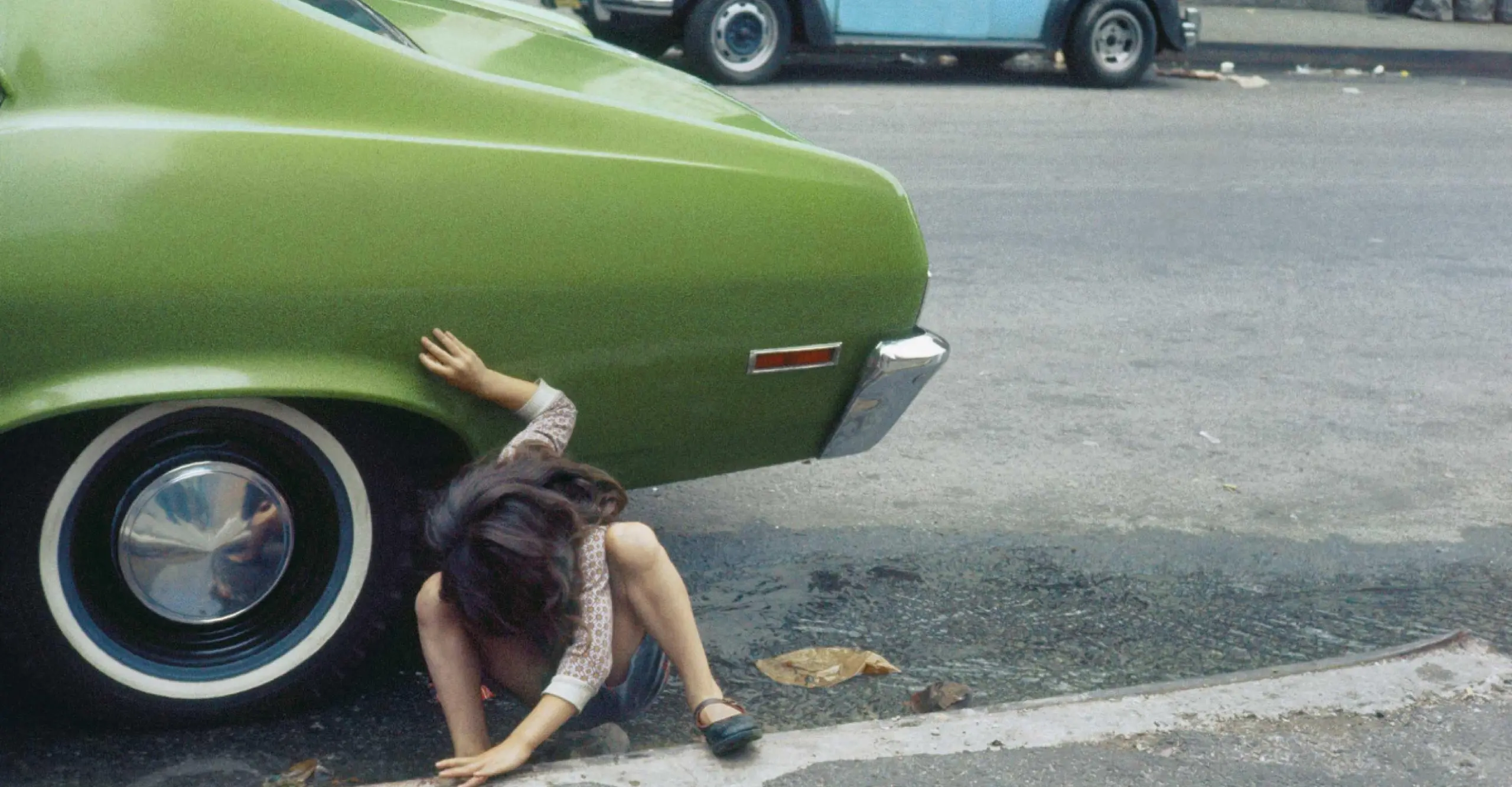 Child squatting looking under a green car