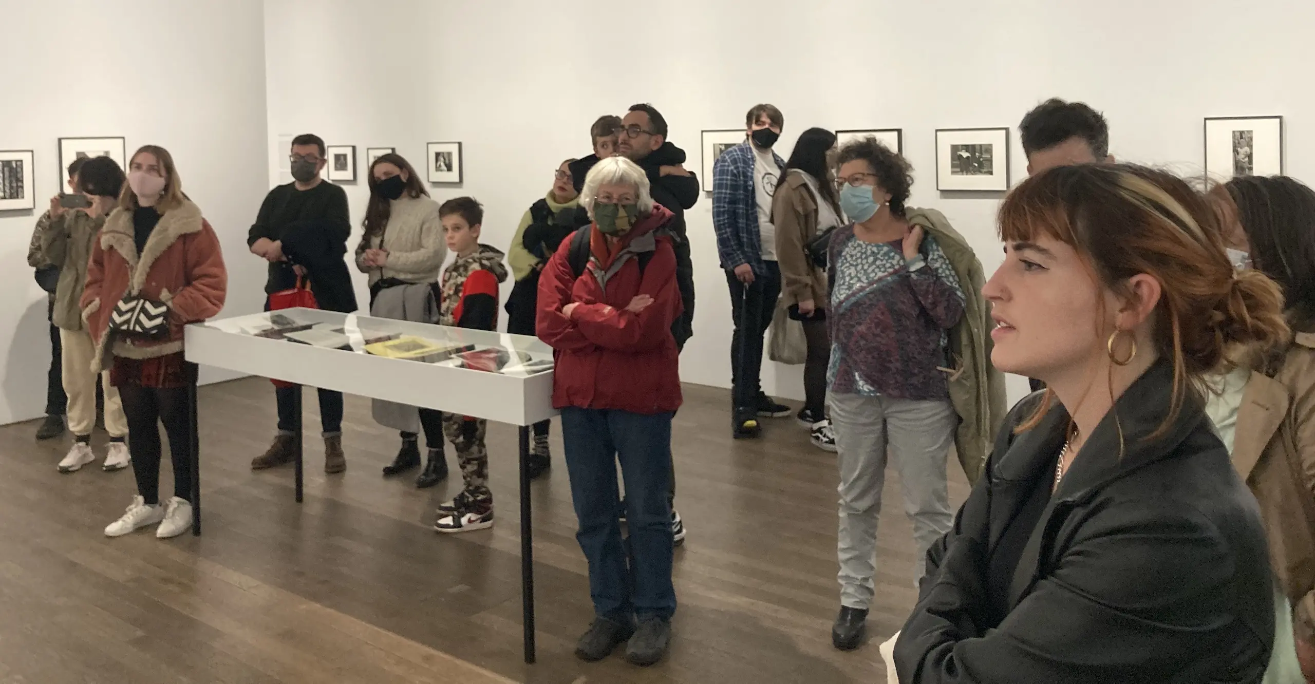 A group of people in a gallery stand facing a speaker during a tour.