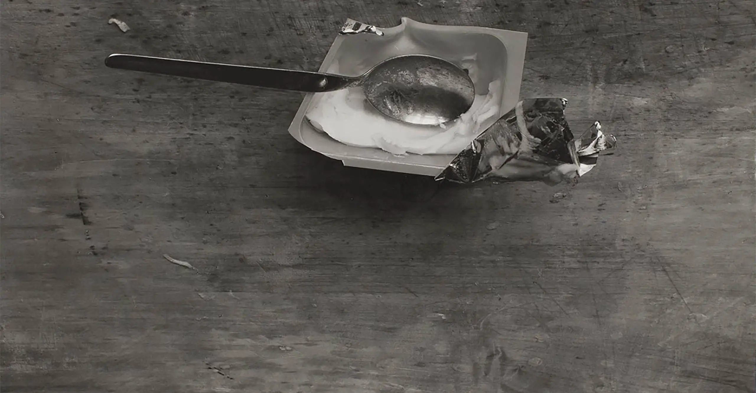 A black and white photograph of a spoon on a wooden table.