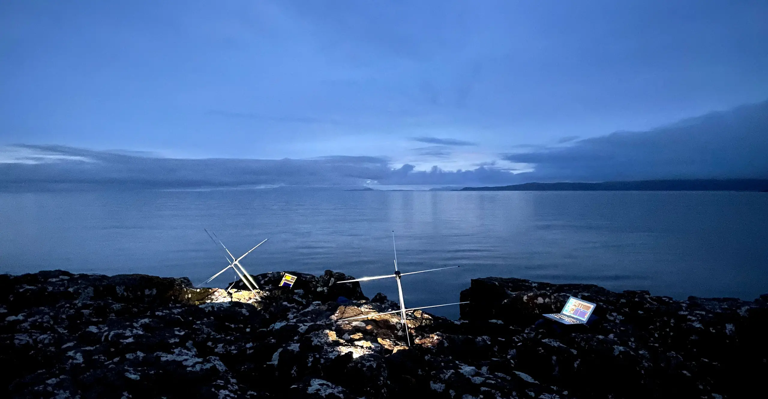 Two antennae and a laptop on the edge of the Isle of Mull at dusk