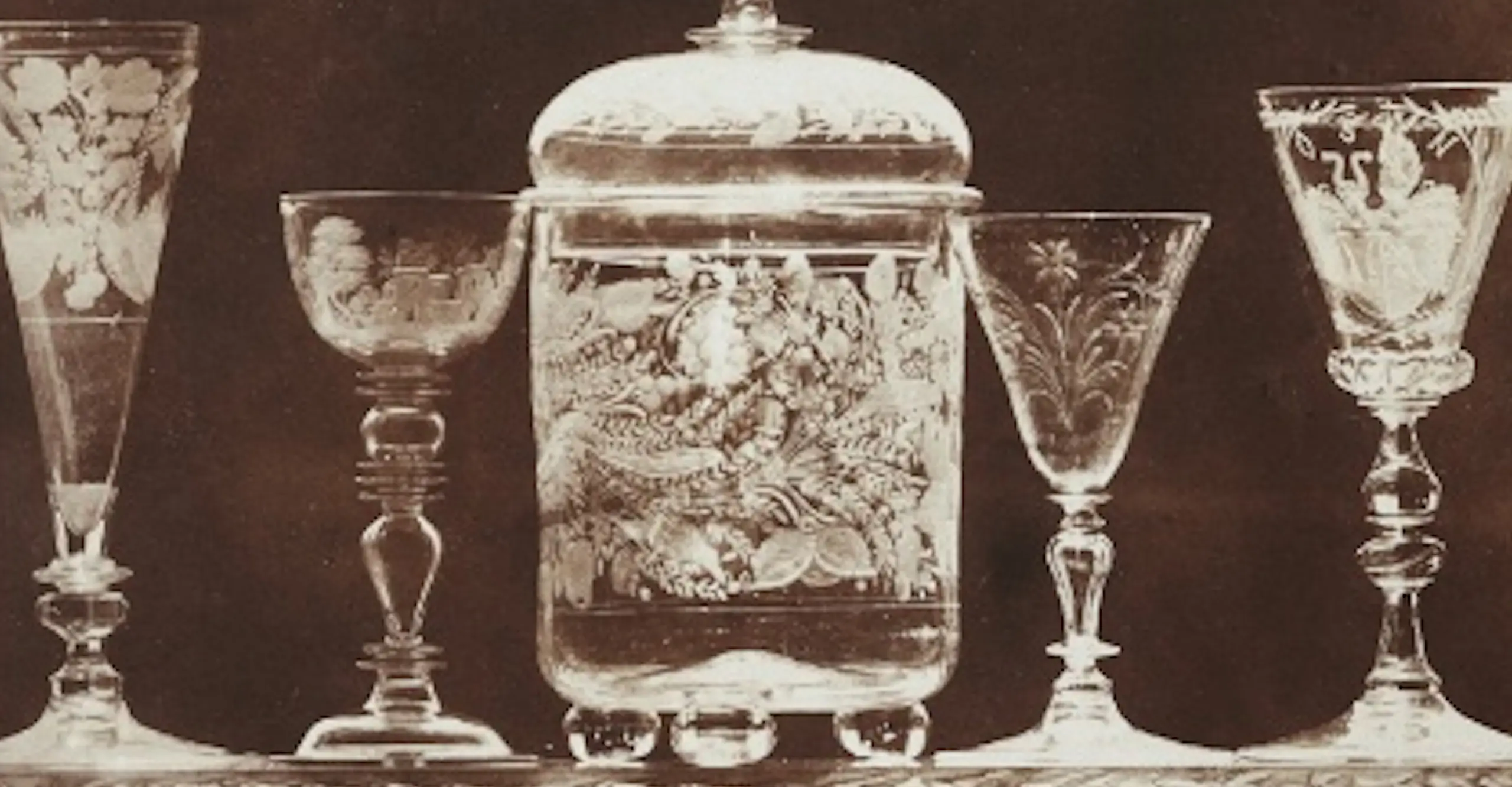 A brown monochrome photograph of sherry glasses and other glassware lined up on a shelf.