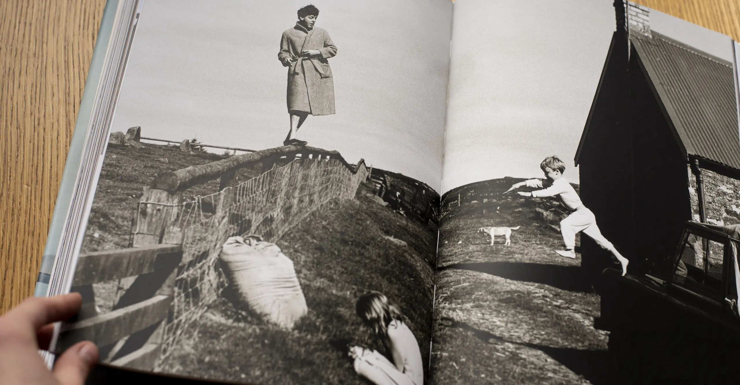 A photograph of a book laid out on a wooden table with a black and white photograph displayed of a man walking on a fence.