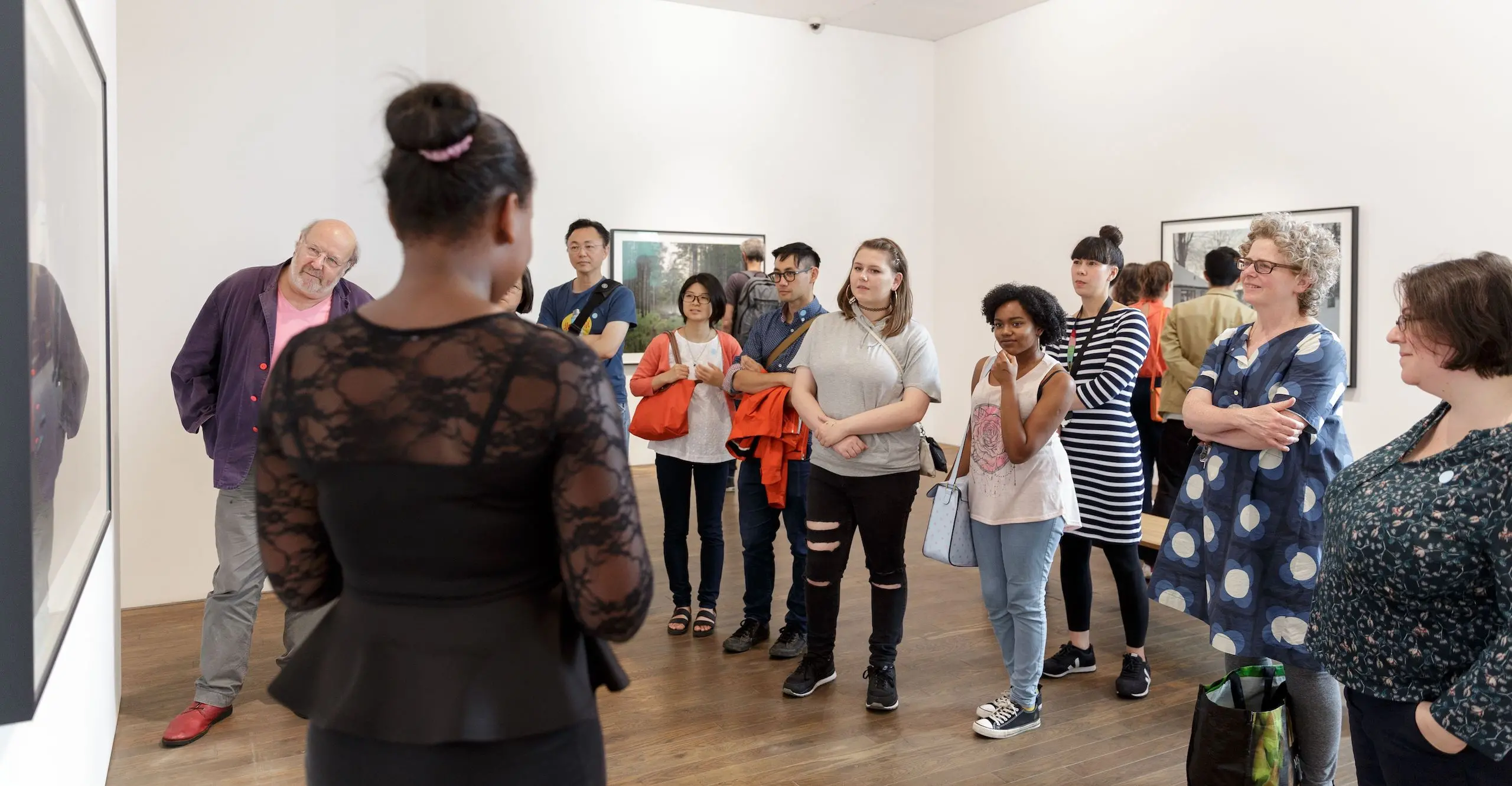 A group of people in a gallery stand facing a speaker during a tour.