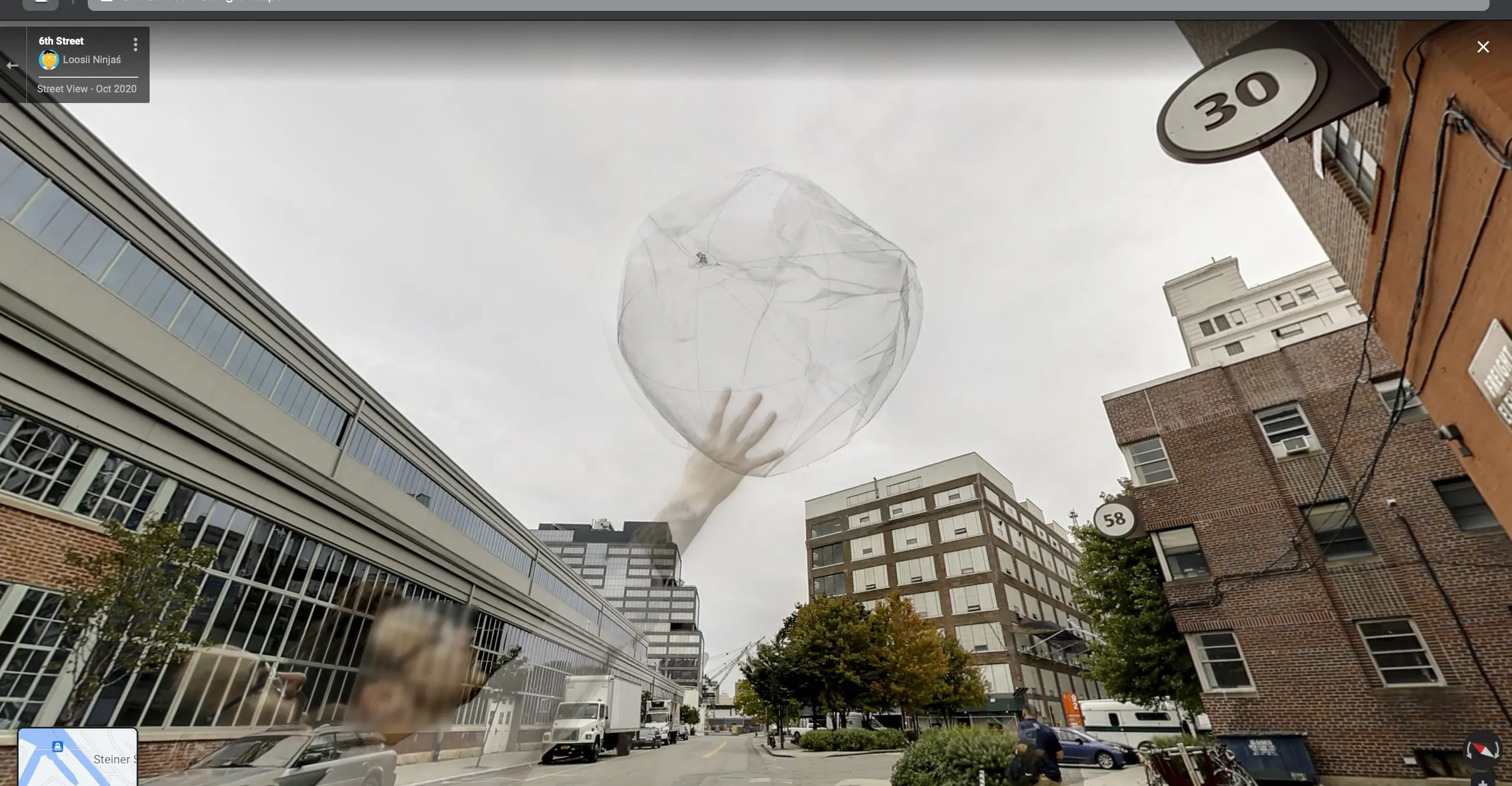 A screen capture of a person holding a balloon in front of a building on the side of a street on Google Street View