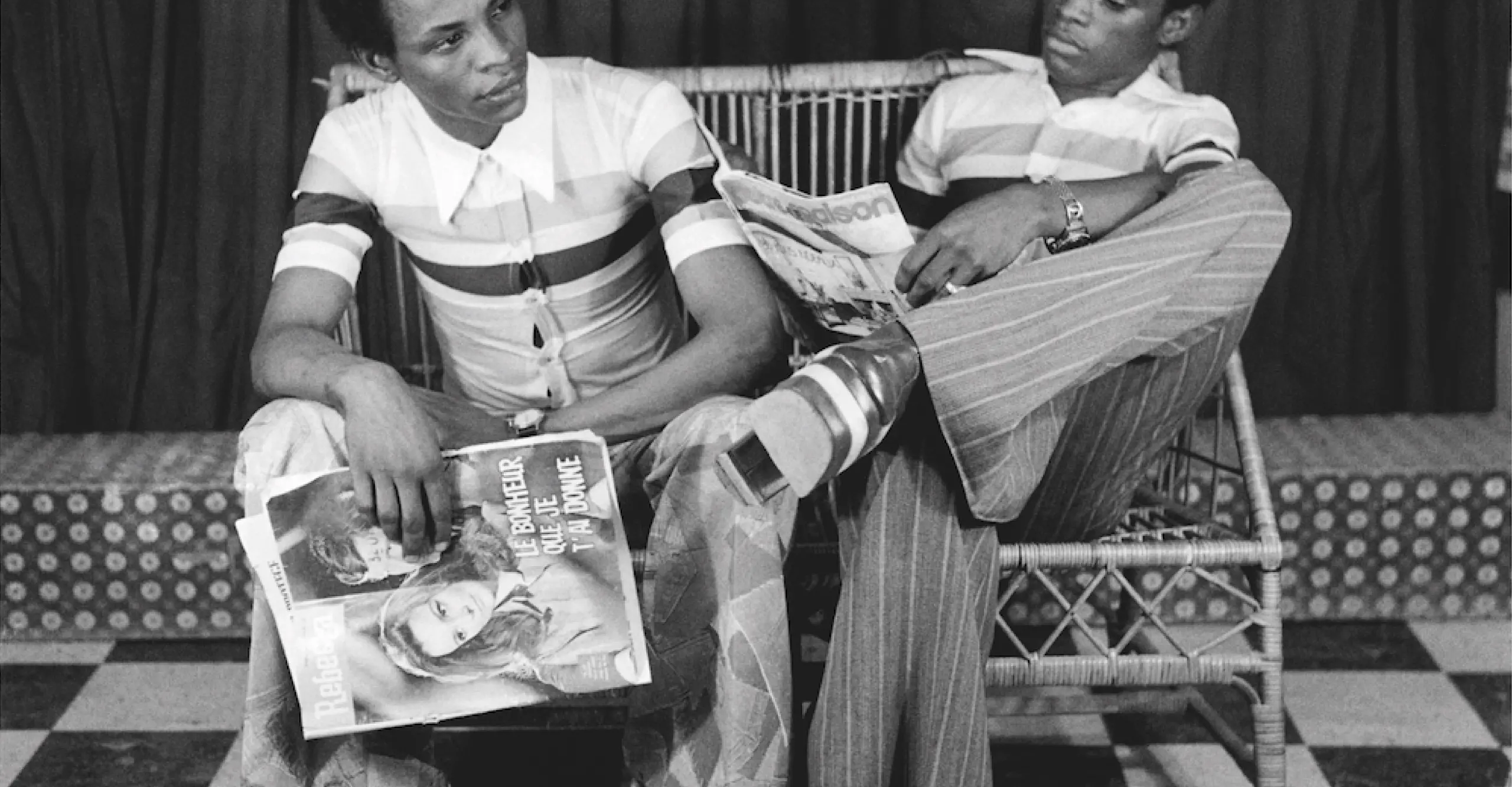 Black and white photo of two Black men seated on a bench in a studio portrait