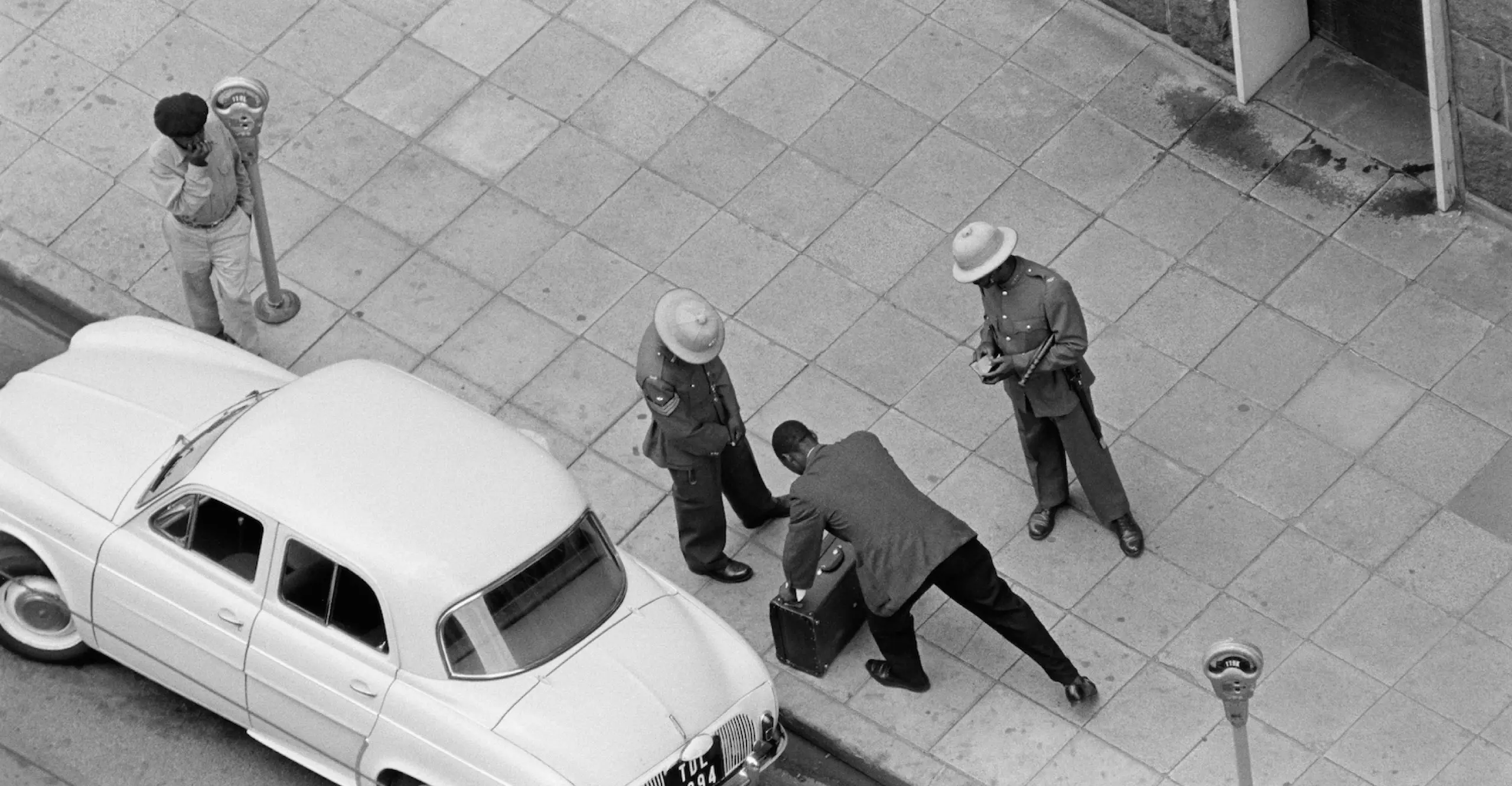 Black and white photograph of five young black men standing and staring off into the distance. One of them holds a document in his hand.