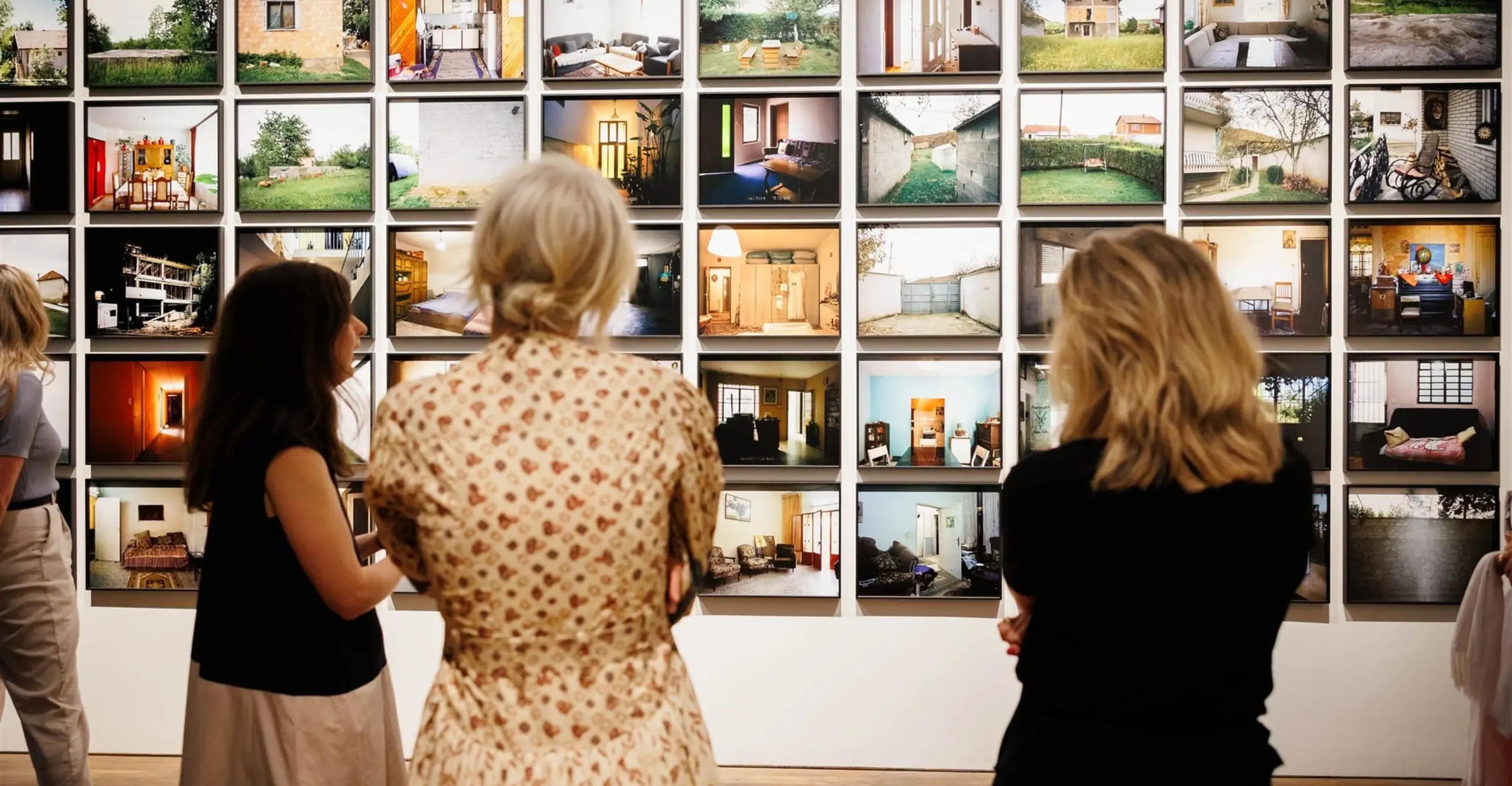 The backs of three women who are viewing a wall of displayed photographs.