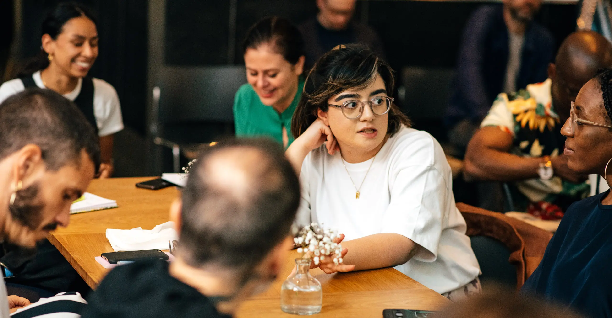 Photo of people sitting together at tables talking, listening and laughing