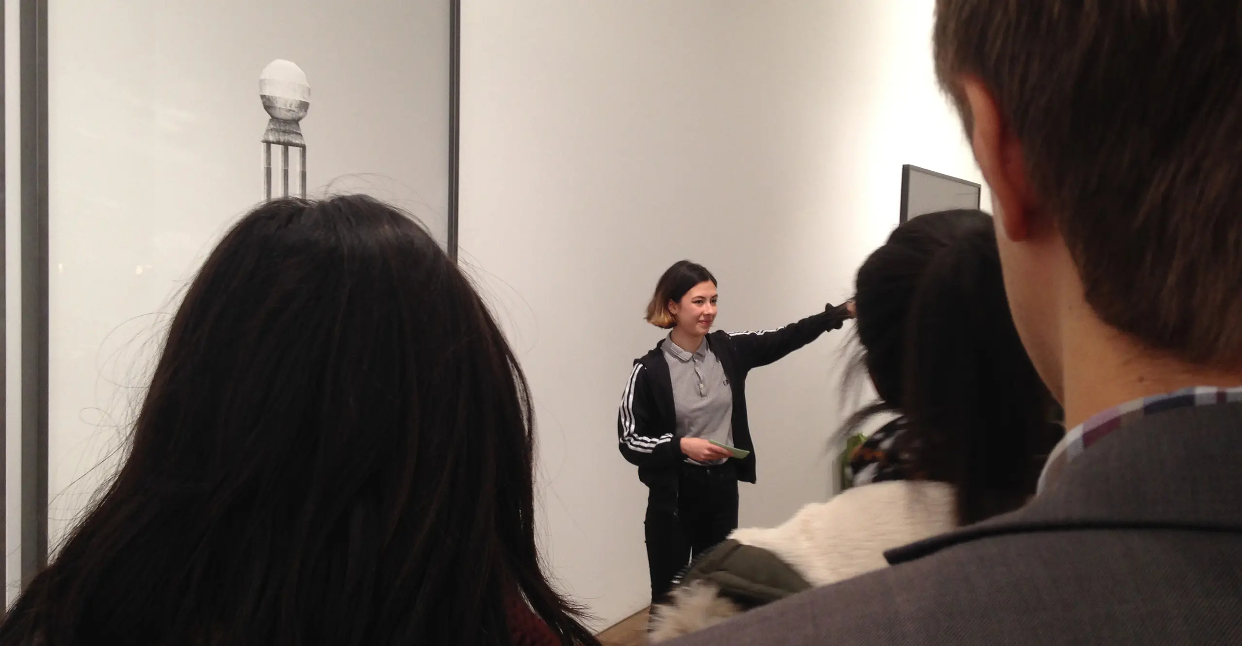 A young person stands in the middle of frame in front of a photograph on a wall.