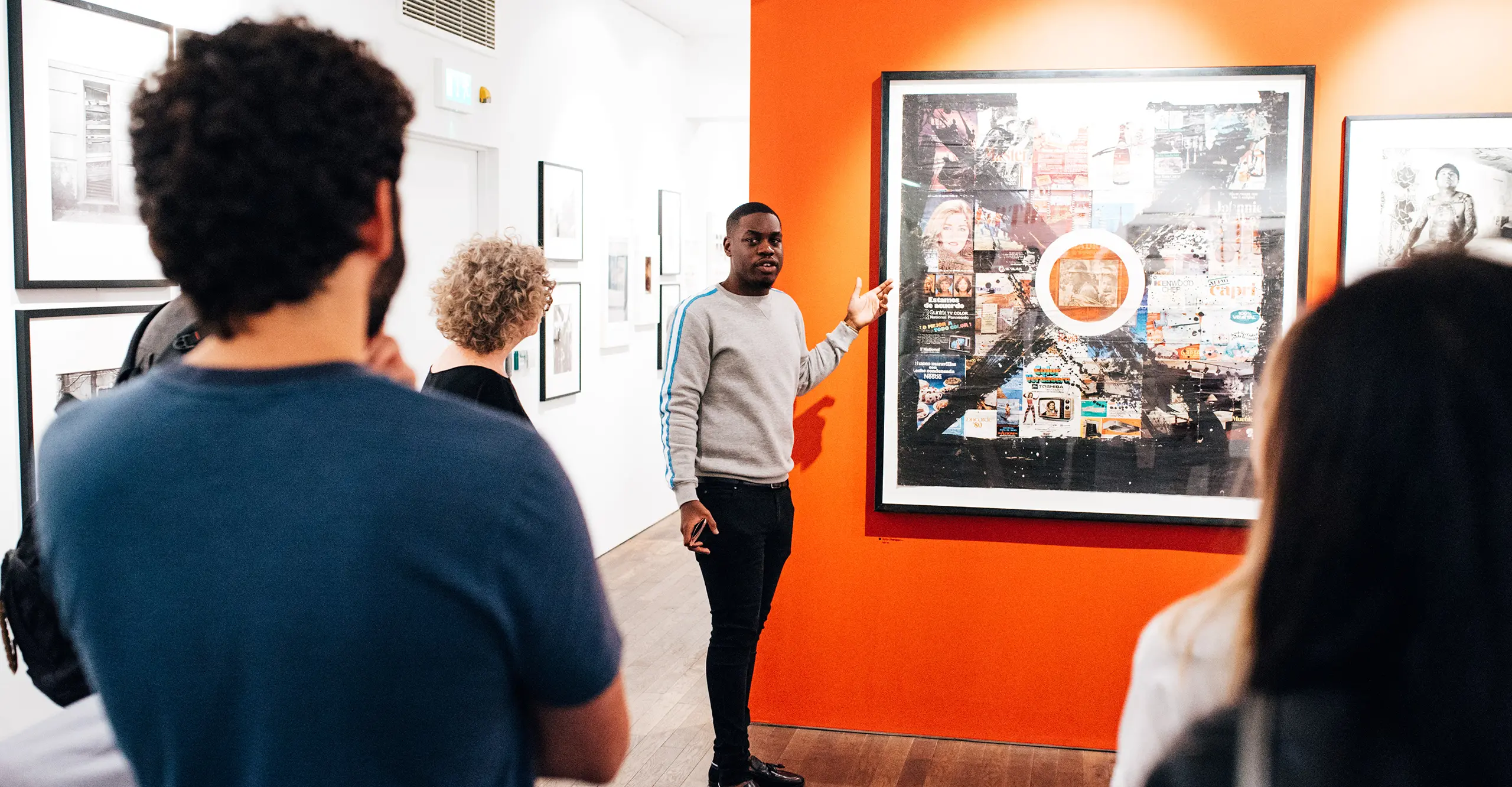 A person stands in front of a large framed photograph with audience members standing to each side. 