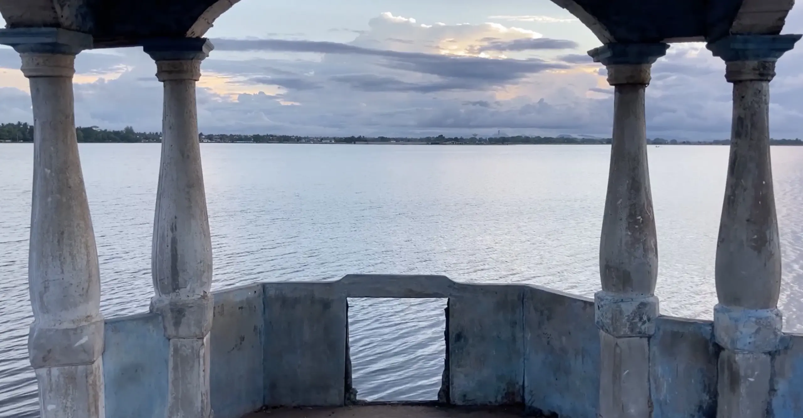 Film still featuring sea view from a balcony with two columns on either site of the picture plane