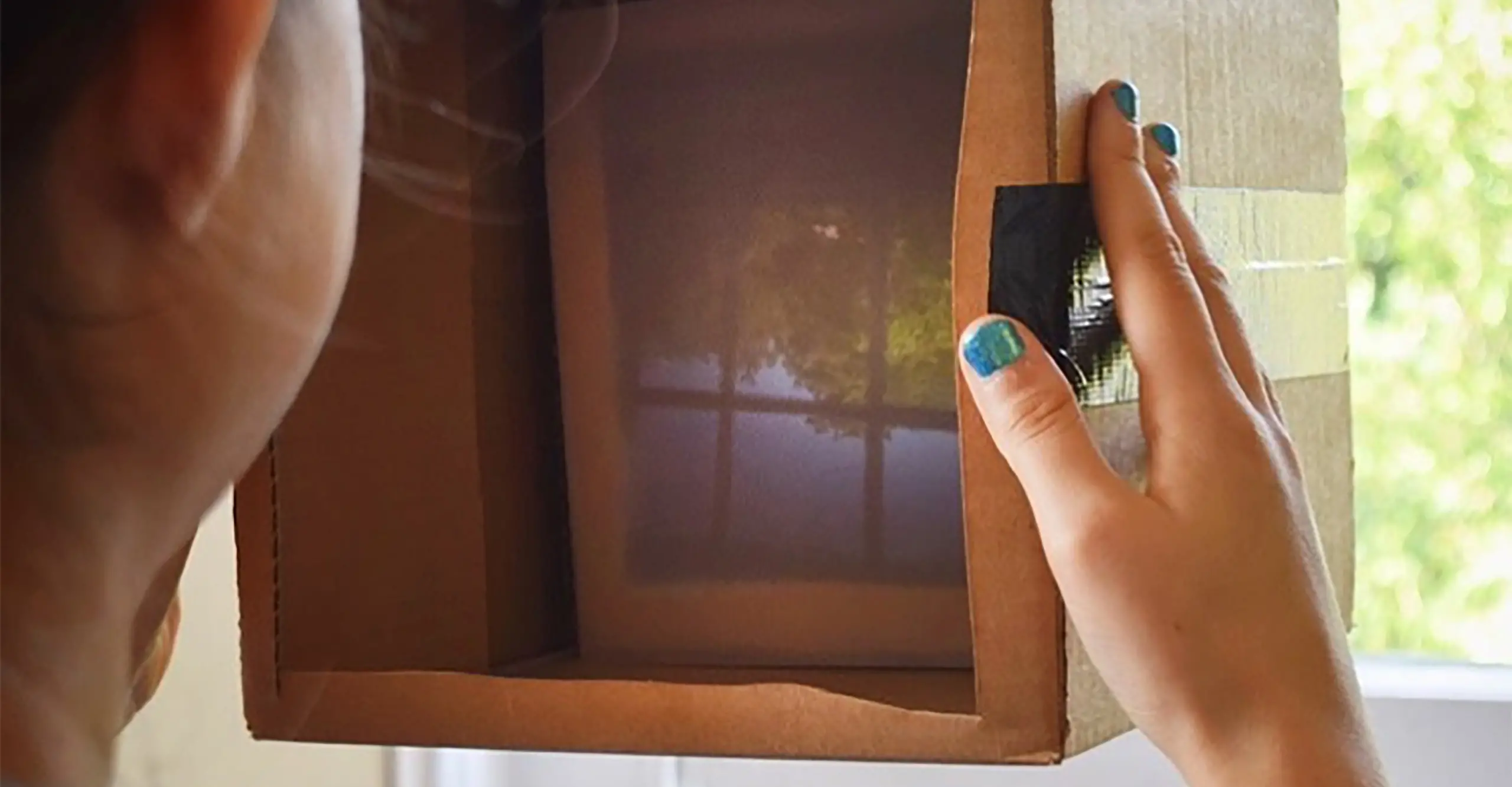 Person looking holding up a square cardboard box to a window. 