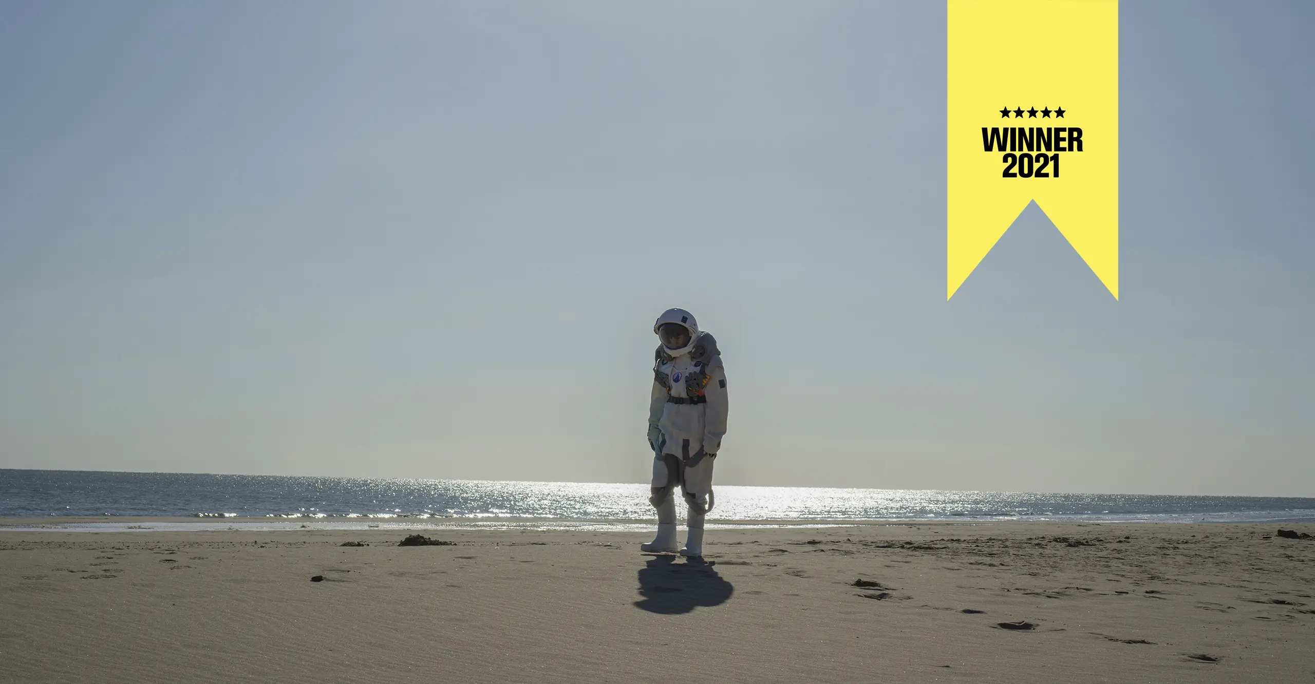 An astronaut stands alone on a beach