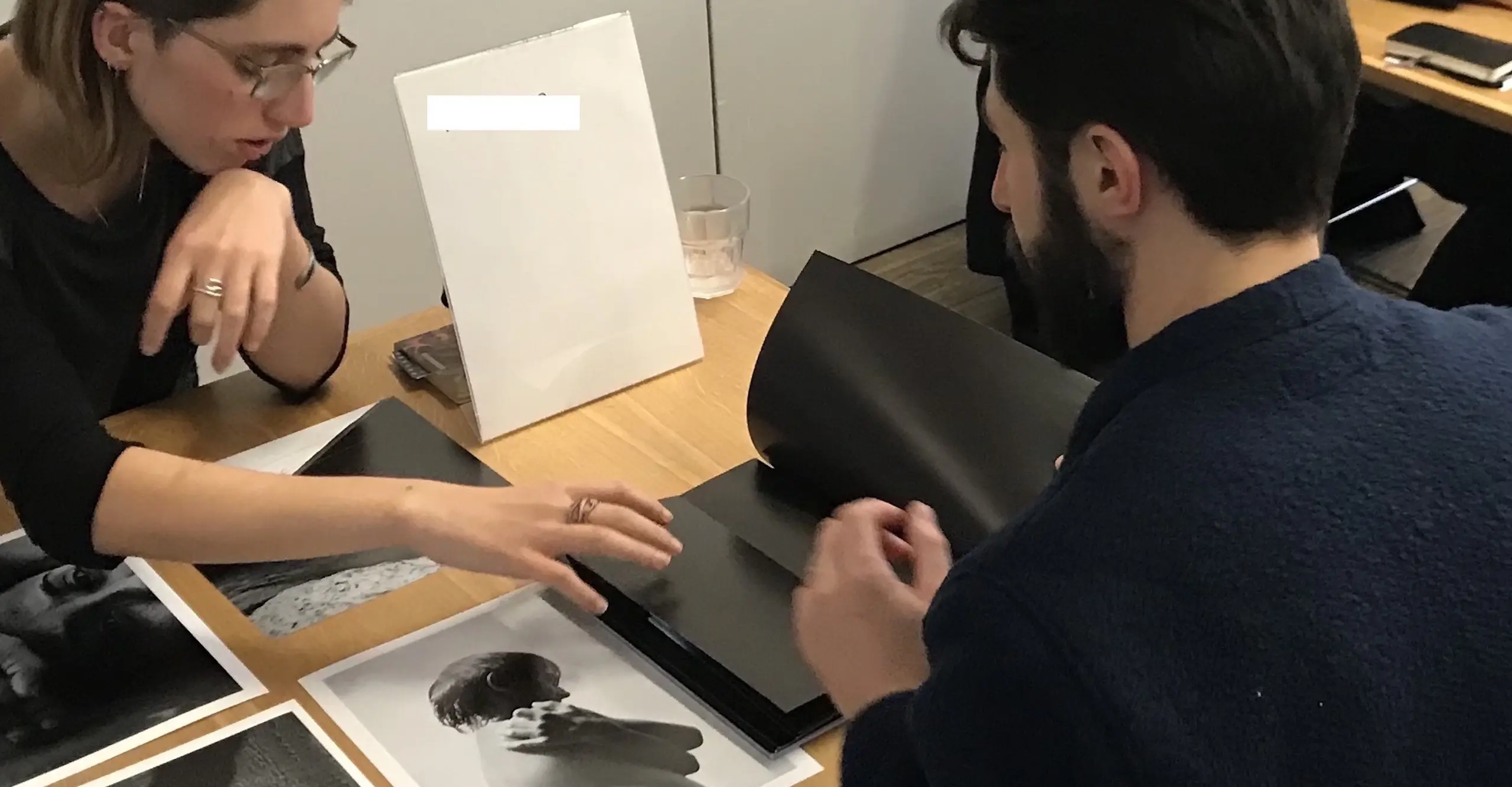 Two people sit across from each other discussing the photographs in front of them on a table.