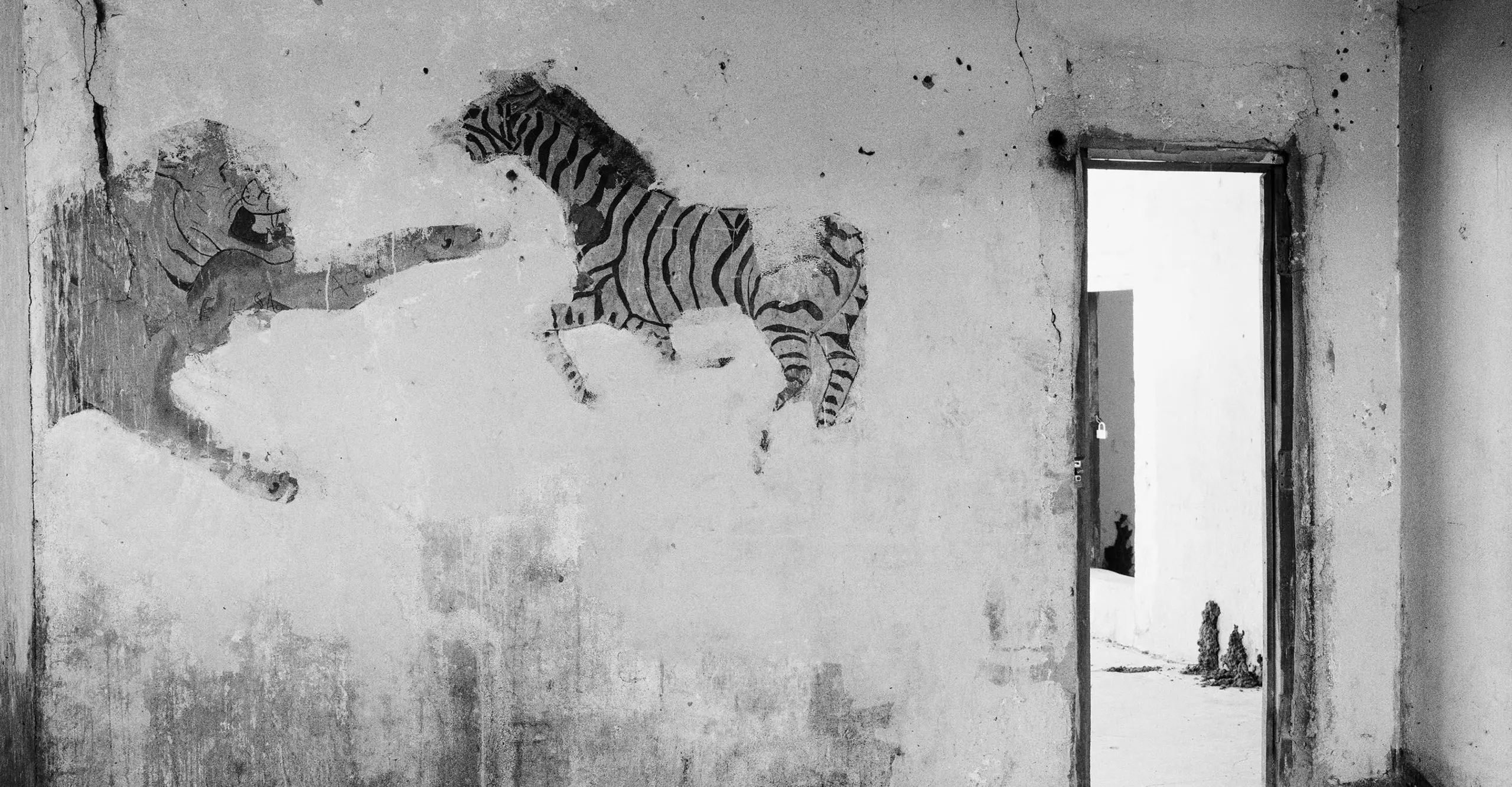 Black and white photograph of a room with a doorway with mural featuring a tiger and zebra on the wall